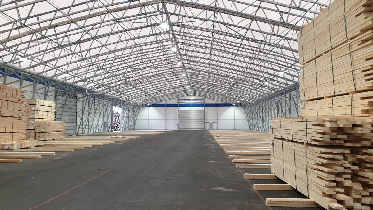Hallgruppen har byggt en rymlig lagerhall med robust stålram, fylld med trästaplar på båda sidor och en stor tom yta i mitten.