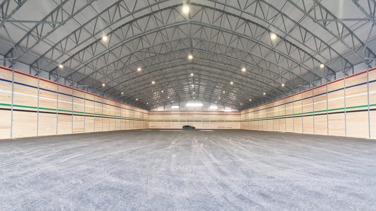 Insidan av en enorm bulkhall med träpaneler och synliga stålbalkar. Denna robusta hall är perfekt för industriell användning, levererad av Hallgruppen.