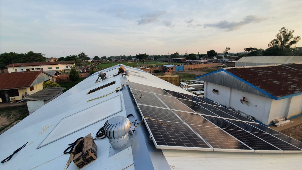 Solpaneler installerade på taket av en haguhall, omgiven av en bymiljö under en klar kvällshimmel.