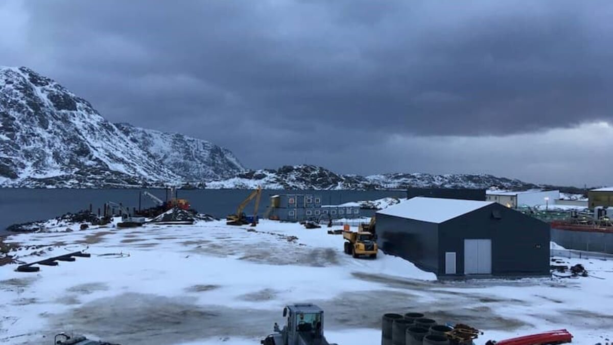 Ett hamnlager tält i ett snöigt landskap vid kusten, med byggutrustning i närheten. Denna hållbara struktur är tillhandahållen av Hallgruppen.