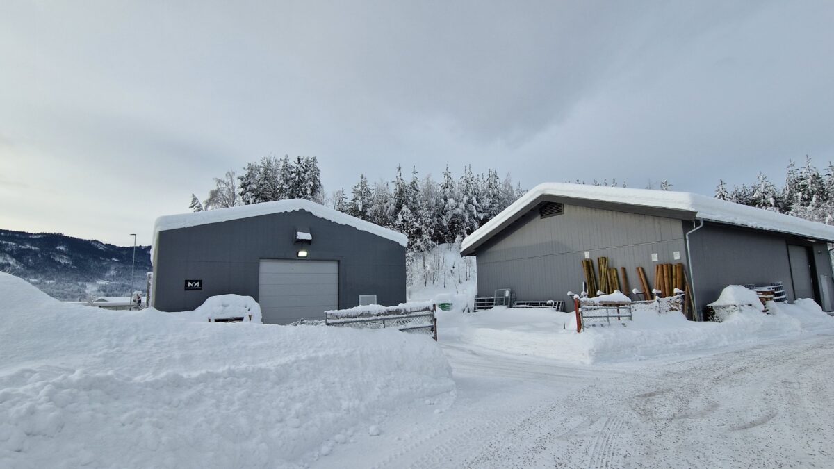 Två grå lagerhallar täckta med snö, omgivna av vinterlandskap. Byggnaderna är uppförda av Hallgruppen.
