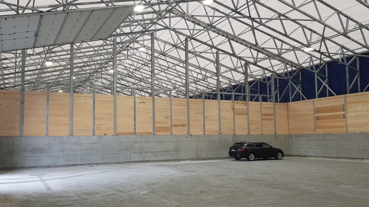 Interiör av en lagerhall med träpaneler, betonggolv och en ensam bil. Byggnaden är uppförd av Hallgruppen.