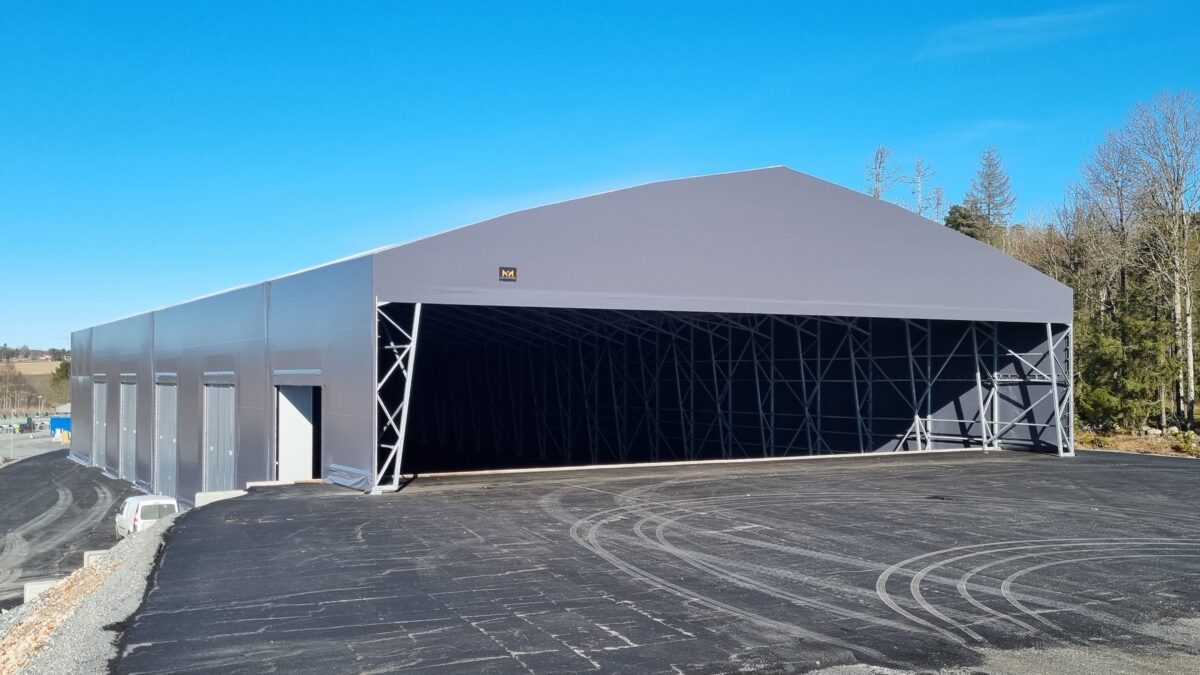 En öppen grå lagerhall vid en byggarbetsplats, byggd av Hallgruppen, med klar blå himmel.