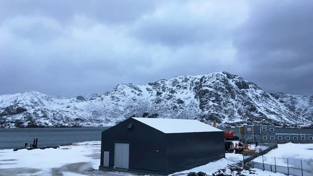 En grå lagerhall omgiven av ett snölandskap, byggd av Hallgruppen, med en bergig bakgrund.