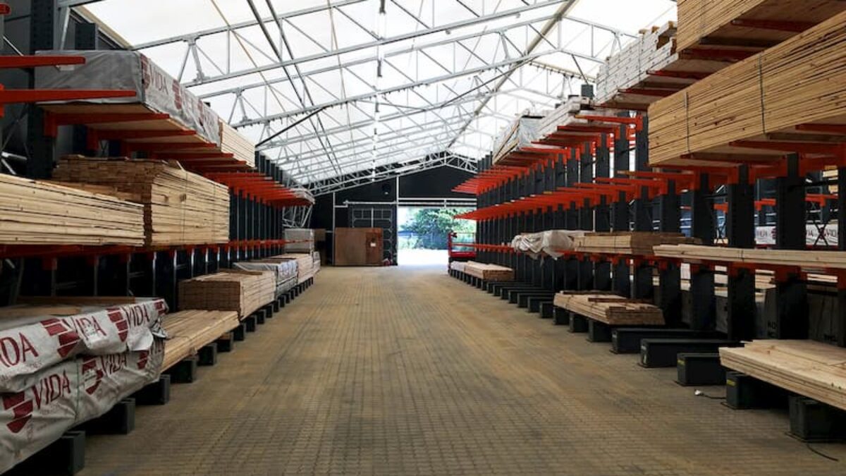 Interiör av en lagerhall med staplade trävaror på båda sidor. Byggnaden är uppförd av Hallgruppen.