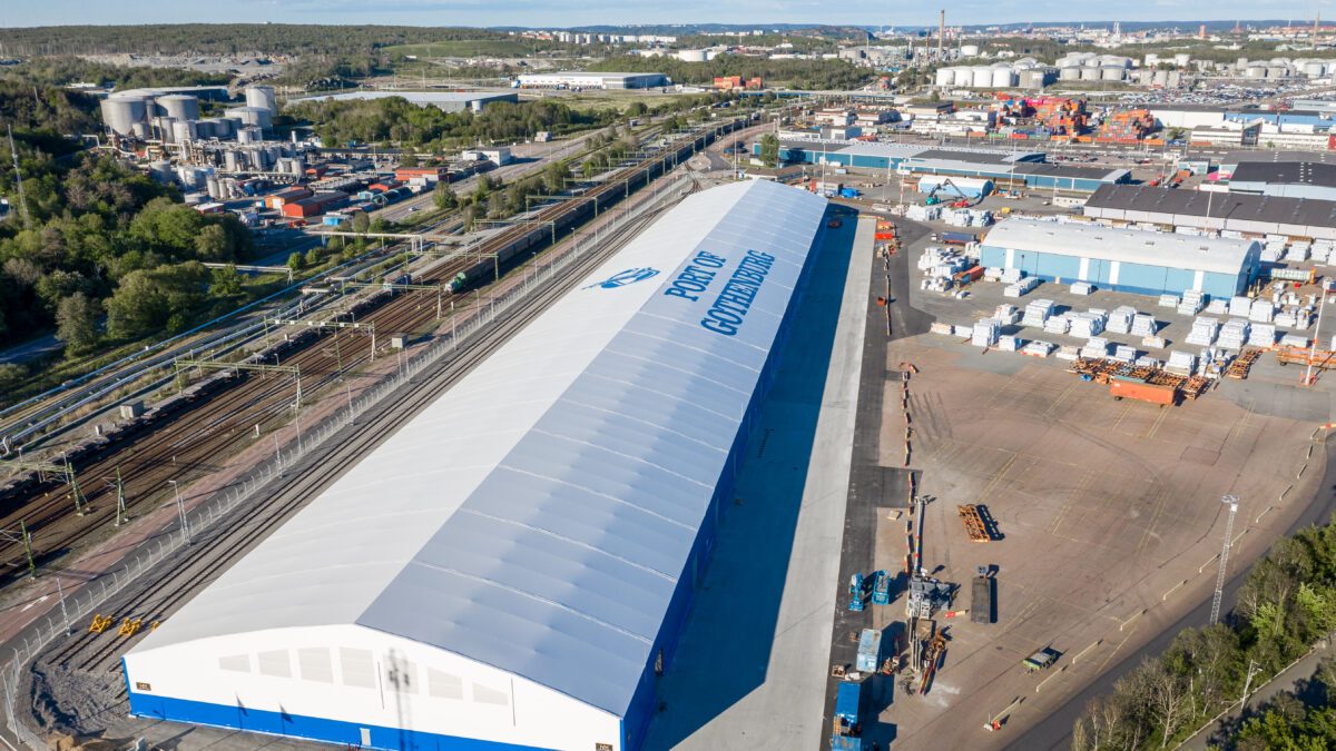En stor vit lagerhall med texten 'Port of Gothenburg' på taket, byggd av Hallgruppen, belägen vid en industrijärnväg.