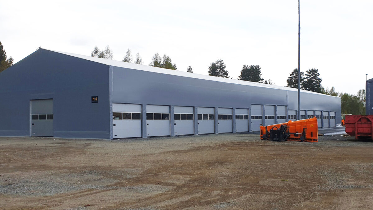 En stor grå hall med flera portar, uppförd av Hallgruppen, står på ett öppet industriområde. Denna byggnad är anpassad för fordon och maskinförvaring.
