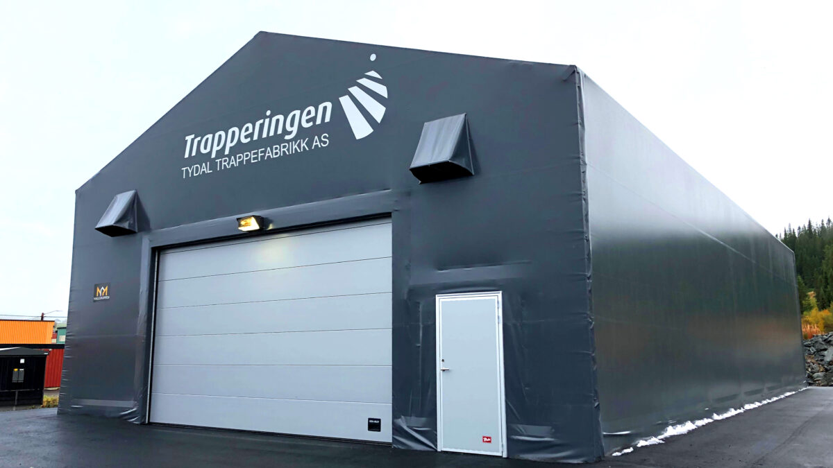 En grå täIthall från Hallgruppen med texten "Trapperingen Tydal Trappefabrikk AS" på fasaden, under en molnig himmel.