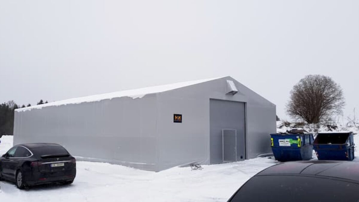 Hallgruppen har byggt en grå täIthall på en snötäckt mark, omgiven av bilar och soptunnor.