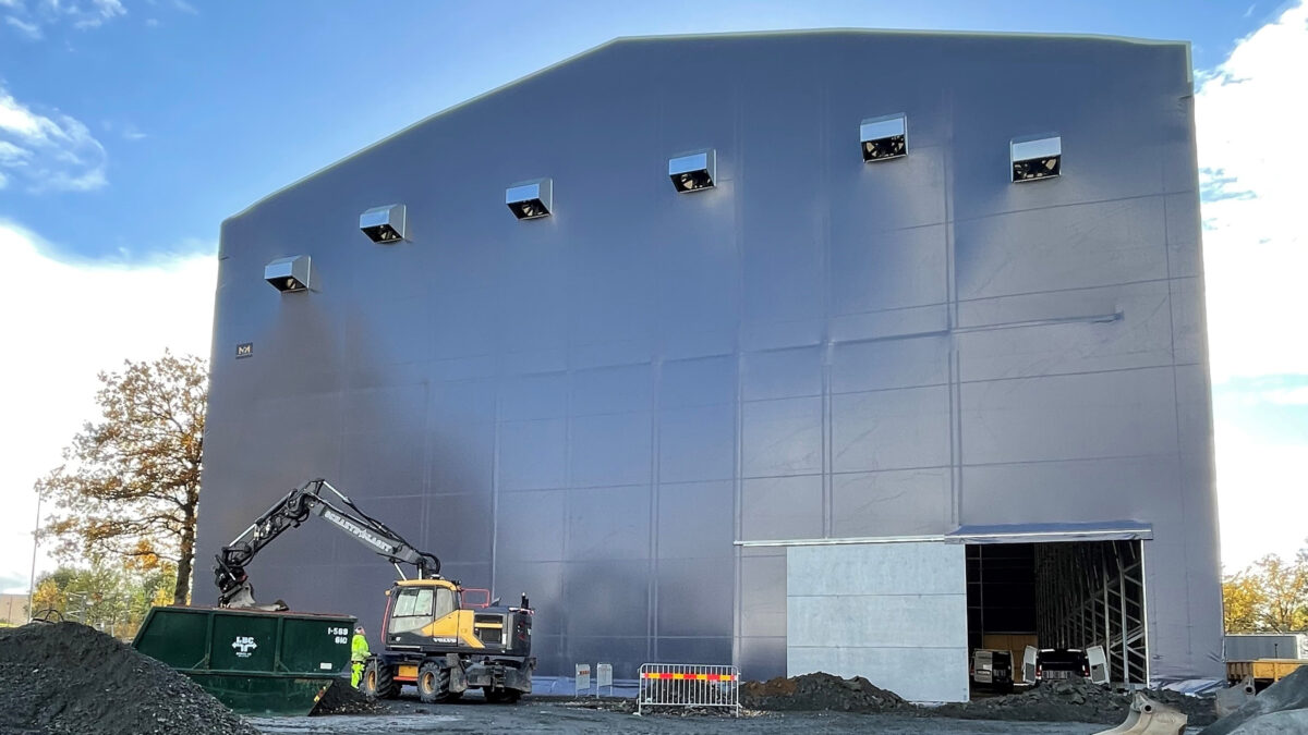 En stor täIthall byggd av Hallgruppen står vid en byggarbetsplats, omgiven av byggutrustning.